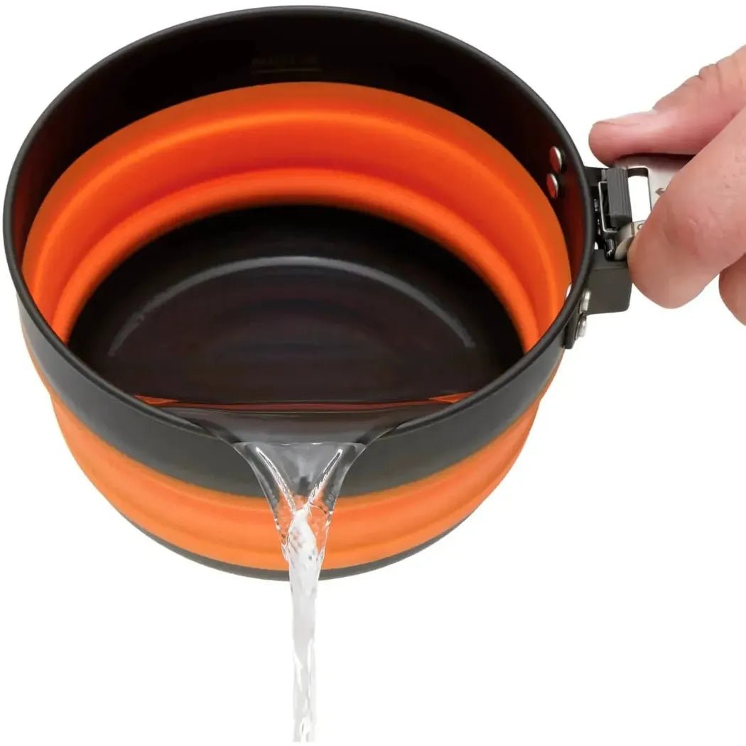 A hand holds the Sea To Summit Frontier UL Collapsible Pot - 1L as water drains from its opening, showing the collapsible orange interior against a white background.