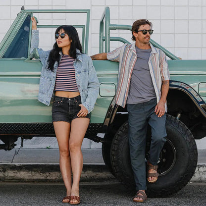 A woman and man in sunglasses stand by a green truck, wearing the Suncloud Barnes Matte Black sunglasses.