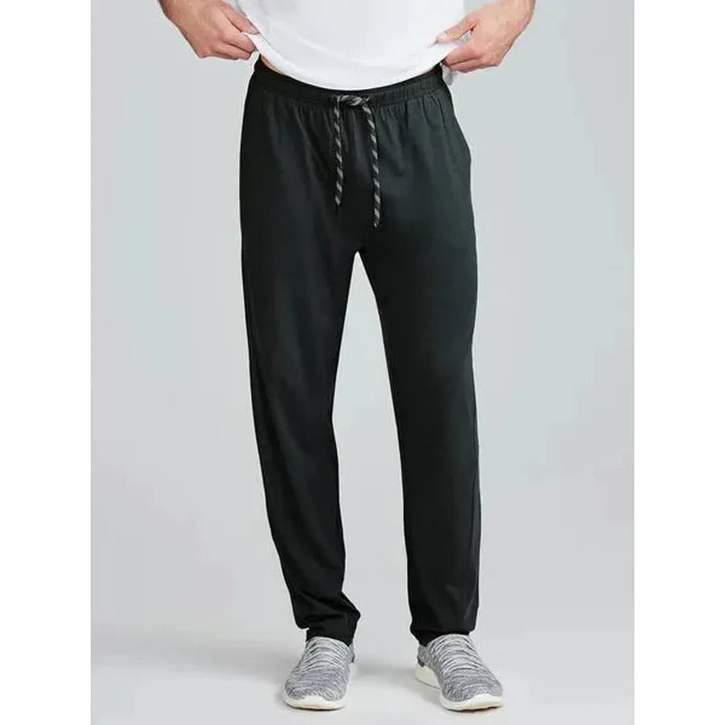A front view of the Tasc Men's Carrollton Classic Pant in Black on a model wearing gray sneakers against a light gray background.