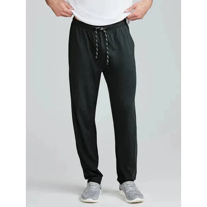 A front view of the Tasc Men's Carrollton Classic Pant in Black on a model wearing gray sneakers against a light gray background.
