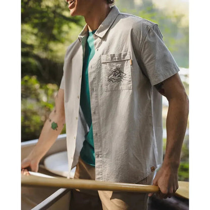 A man wearing the Tentree Men's Hopkins Shirt in Sand Stone Graphite holds a boat oar with a forest background.