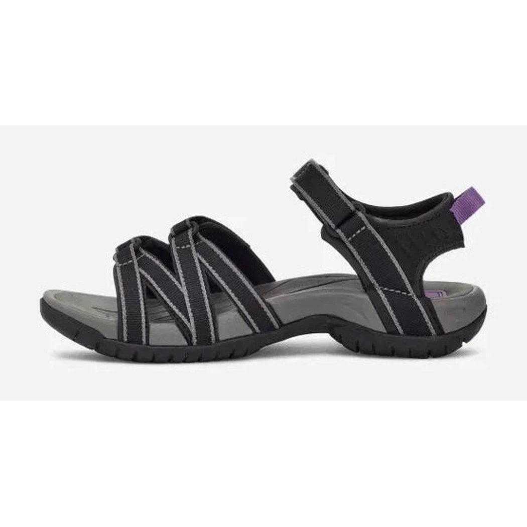 Side view of the Teva Women's Tirra in Black/Grey showing the adjustable strap and purple pull tab against a white background.