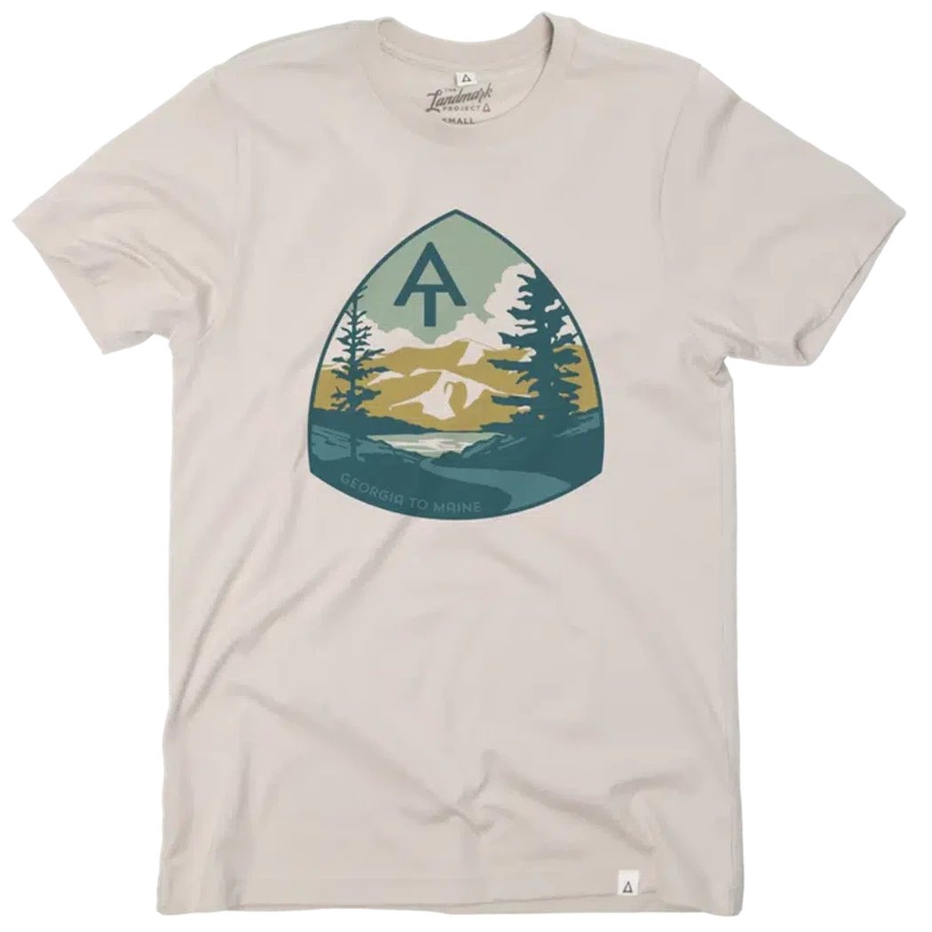 A beige The Landmark Project Appalachian Trail Tee with a triangular graphic of mountains, trees, and a tent logo on the front.
