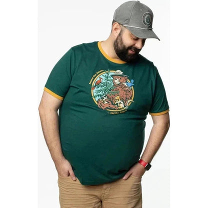 A man wearing The Landmark Project Smokey's Friends Ringer Tee in Spruce + Golden stands with his hands in his pockets against a white background.