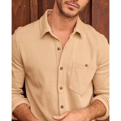 A front view of the Toad & Co Men's Shadowbrook Long Sleeve Shirt in Camel Twill on a model against a wooden background.