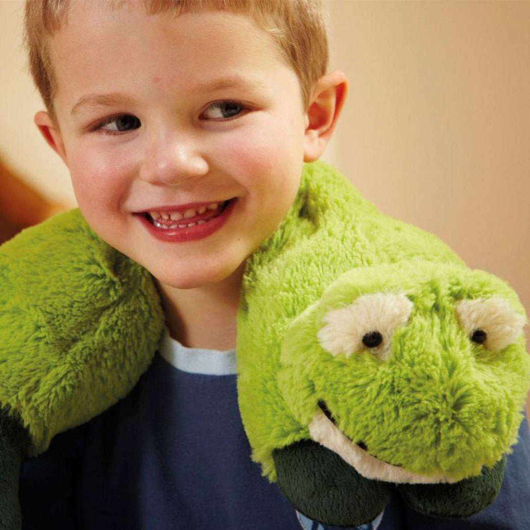 A young boy smiles wearing the Warmies Frog Cozy Wraps, a green plush frog-shaped neck warmer with a smiling face.