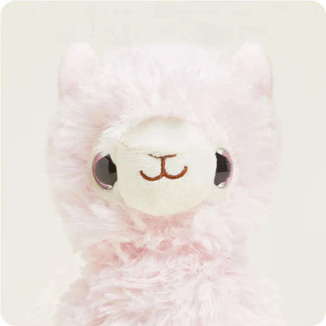 A close-up of the Warmies Pink Llama Junior with large eyes and a soft pink fur texture against a light background.