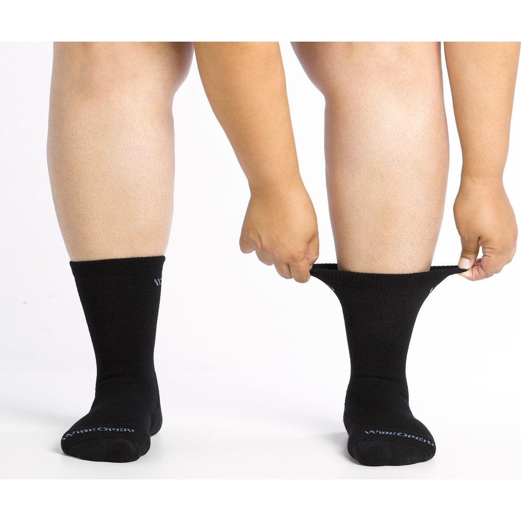Close-up of a model wearing Wide Open Women's Solid Cushioned Crew Socks in Black, pulling the right sock up against a white background.