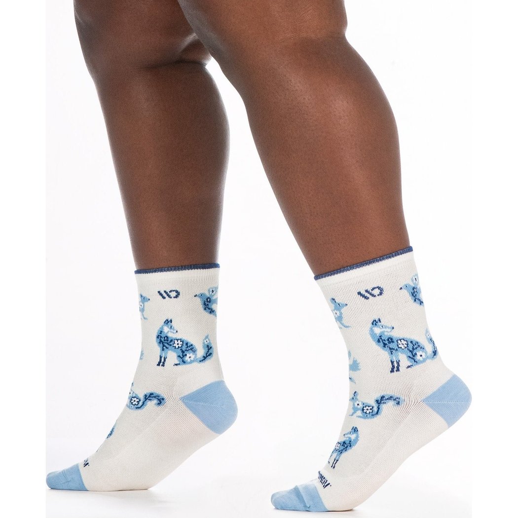 Close-up of a model wearing Wide Open Women's Woodland Wonder No Cushion Micro Crew Socks in Teal with blue fox patterns and light blue heel/toe against a white background.